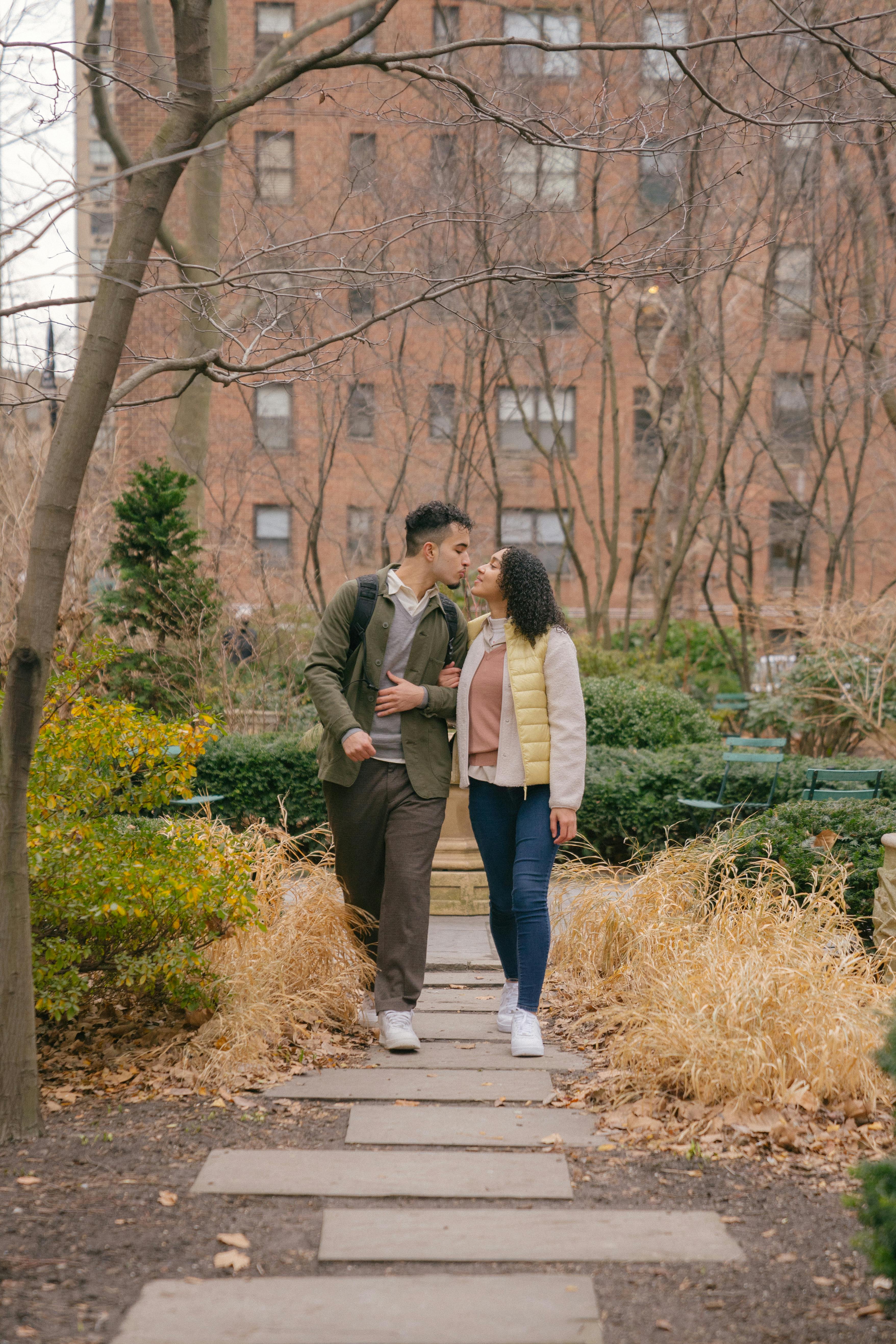 ethnic couple having date while walking in park and kissing