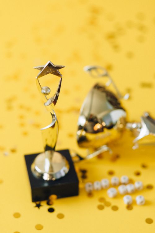 Free Golden star award trophy with confetti on yellow surface, symbolizing success and achievement. Stock Photo