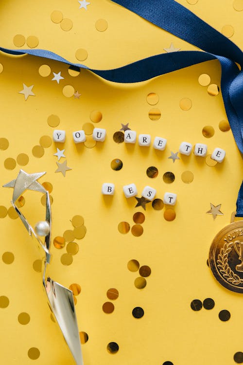 Dice with 'You Are the Best' Message on Yellow Background Beside Medal on Ribbon and Statuette