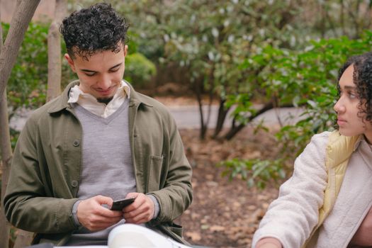 Concentrated Hispanic girlfriend looking at cheerful boyfriend using smartphone