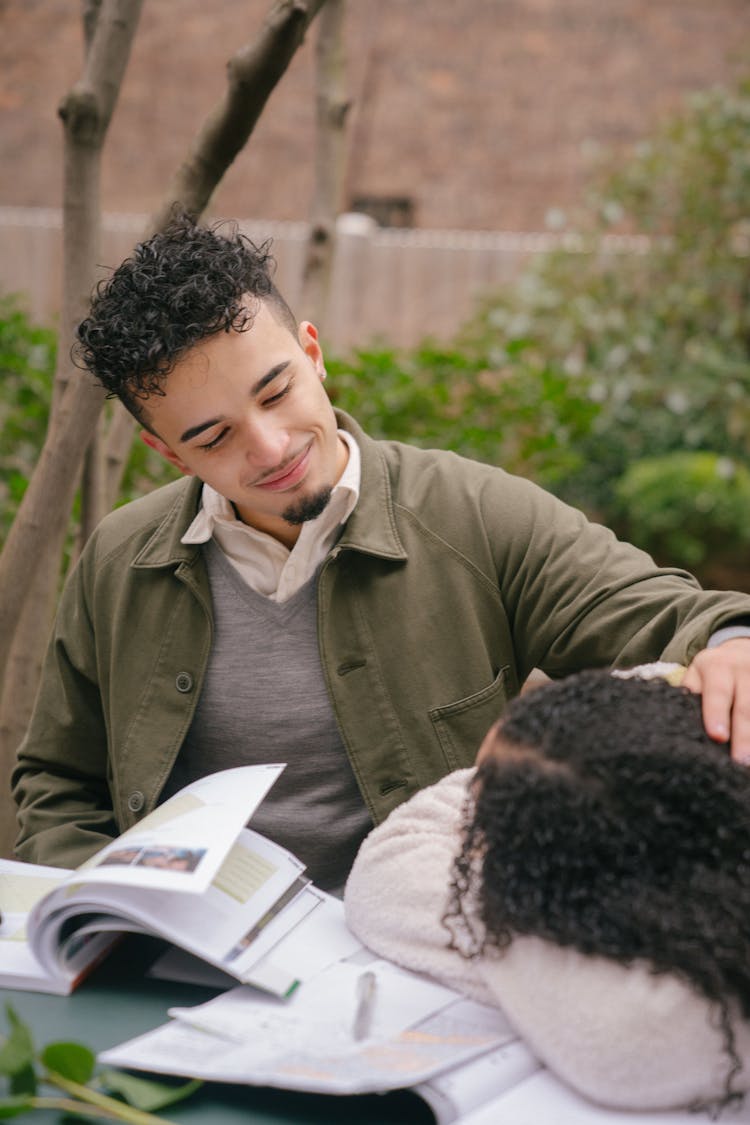 Happy Hispanic Boyfriend Embracing Tired Girlfriend Lying At Table