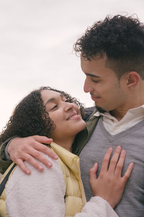 Happy ethnic couple with curly hair hugging and smiling while looking at each other on white background