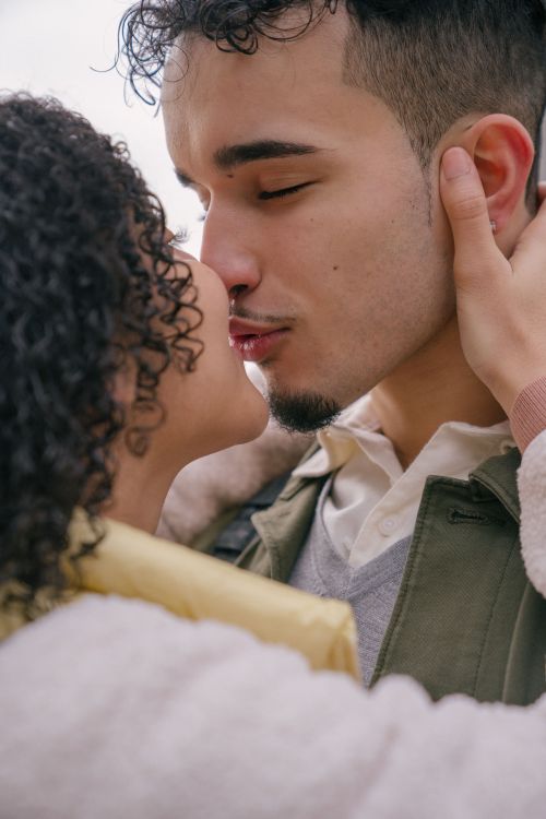 Free Cheerful young Hispanic couple in casual clothes embracing and kissing each other against light background in daytime Stock Photo