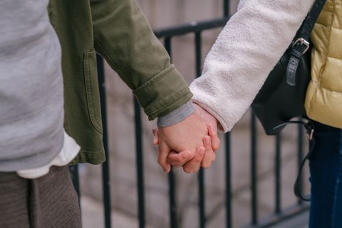 Free Crop anonymous couple in casual clothes standing on street near metal fence and holding hands together in daylight Stock Photo
