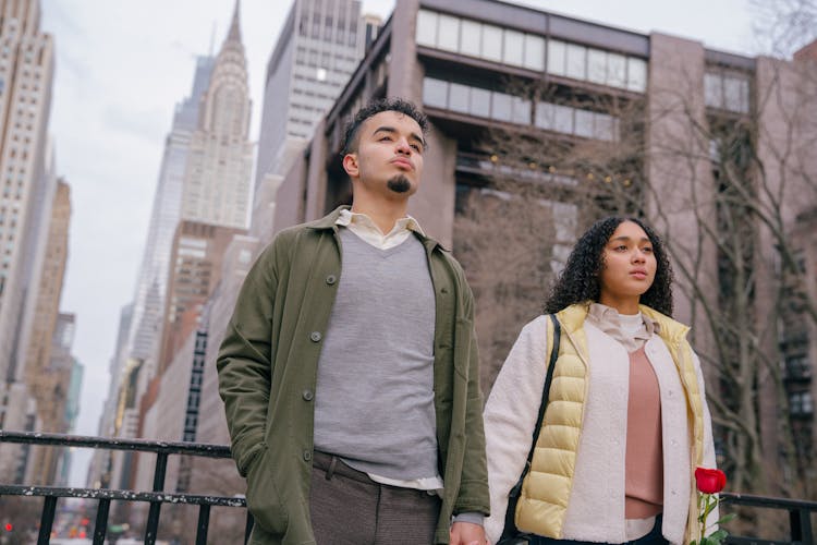 Serious Hispanic Couple In Trendy Clothes Standing On Street Against Building