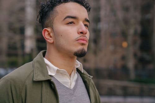 Crop self assured bearded young Hispanic male millennial in casual clothes standing on street and looking away thoughtfully