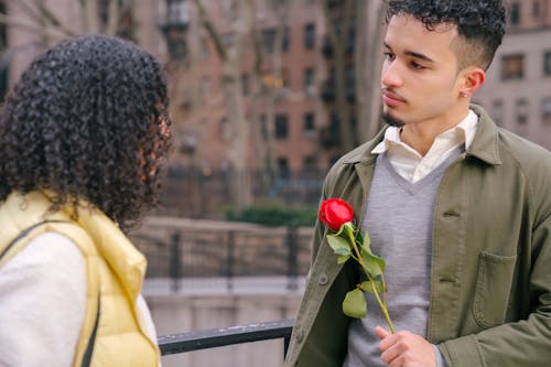 Free Crop romantic young Hispanic guy in casual clothes giving red rose to anonymous girlfriend with dark curly hair during romantic date on city street Stock Photo