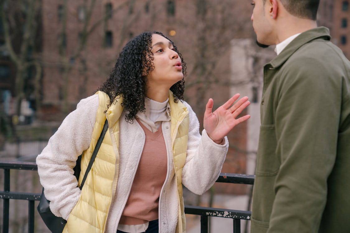 Young stylish Hispanic lady quarreling with crop boyfriend while standing together on city street