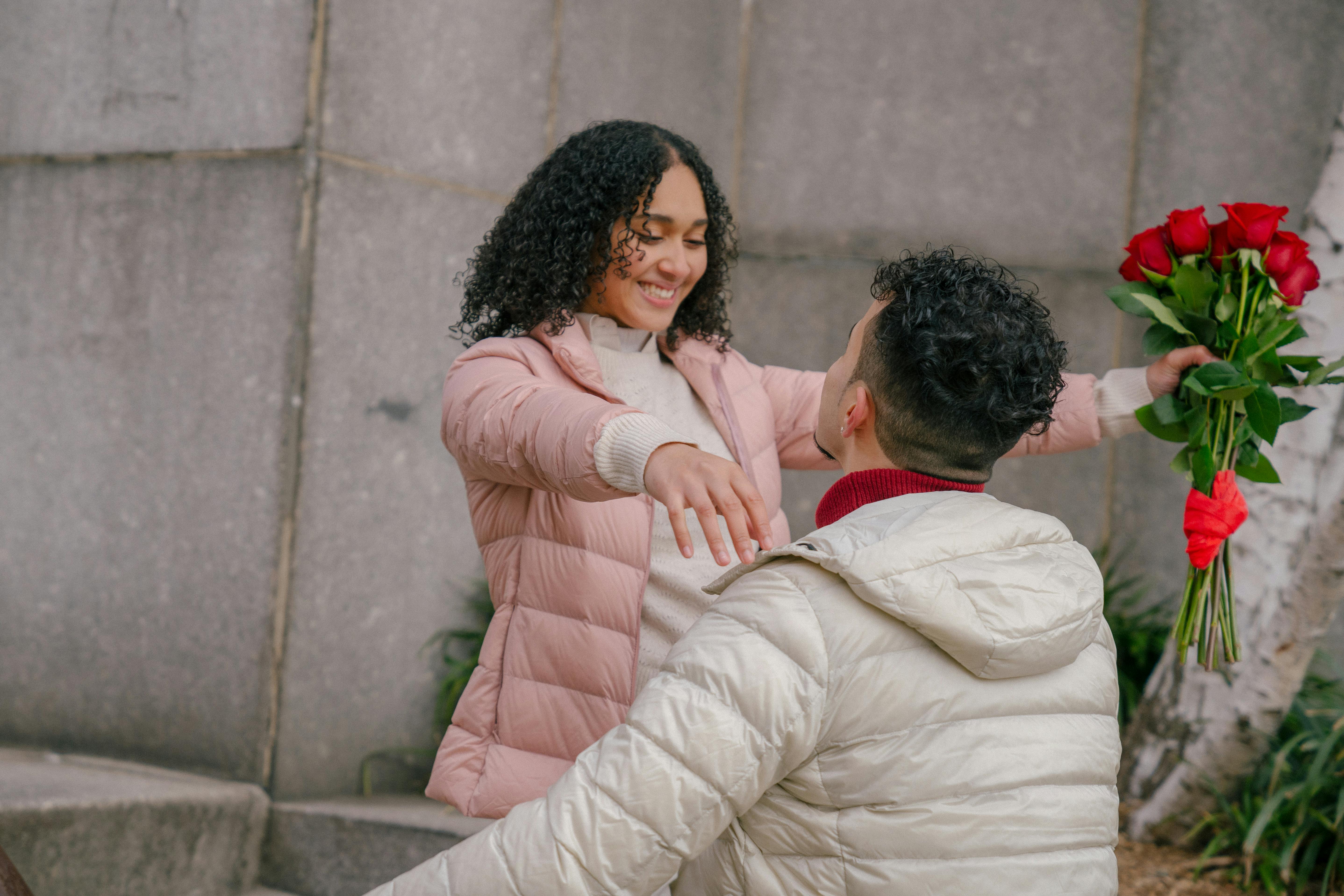 happy hispanic lady hugging boyfriend after receiving bouquet during date