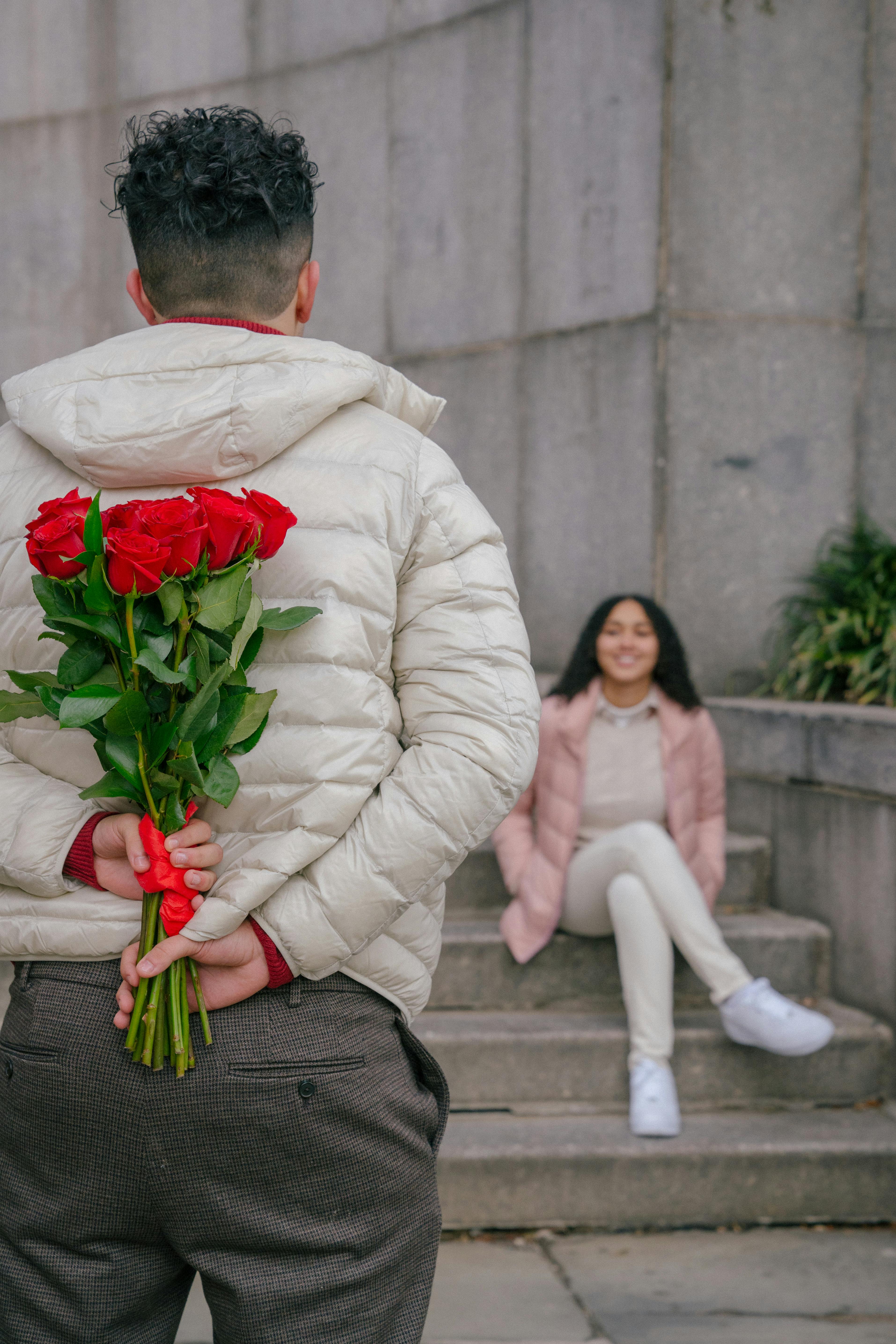 unrecognizable man hiding bunch of red roses behind back before date with happy girlfriend