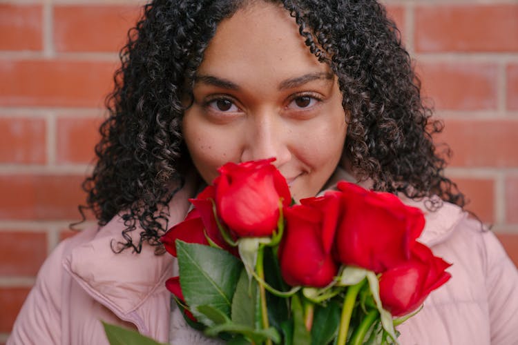 Smiling Young Hispanic Woman Smelling Red Roses And Looking At Camera