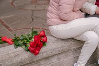 High angle of crop anonymous couple in casual wear sitting on concrete border near bunch of flowers with bow