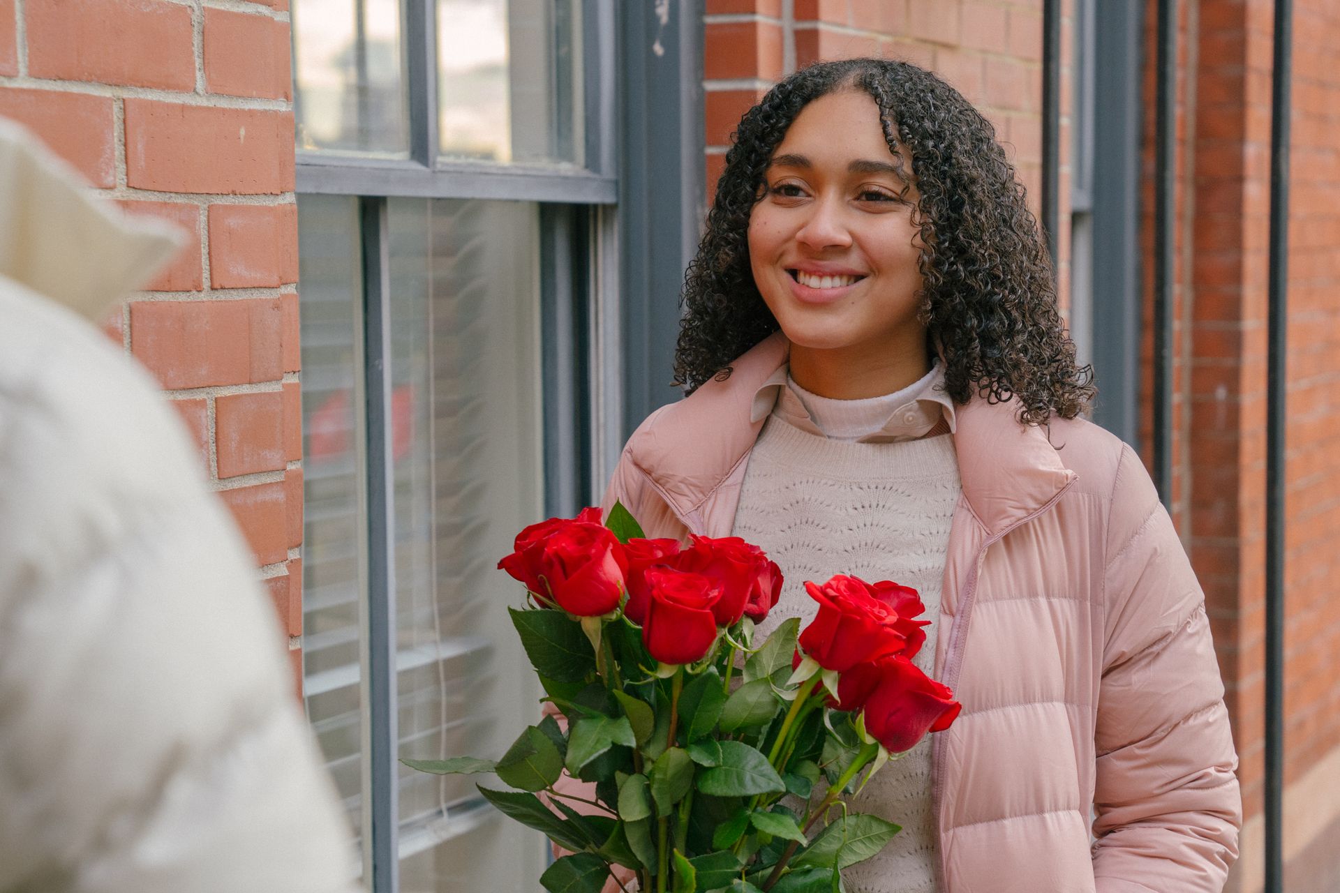 Smiling Hispanic girlfriend with curly hair receiving bunch of fresh flowers from boyfriend for romantic celebration