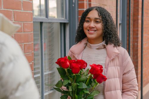 Free Smiling Hispanic girlfriend with curly hair receiving bunch of fresh flowers from boyfriend for romantic celebration Stock Photo