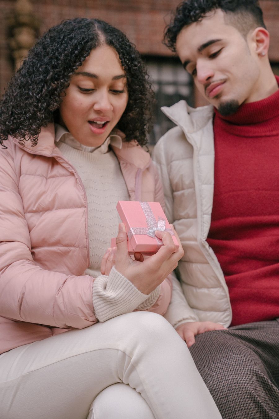 Une personne ouvre un petit cadeau emballé, surprise et souriante