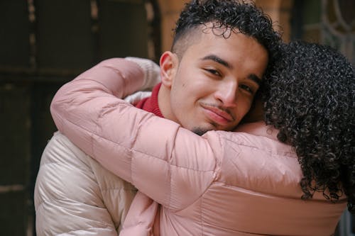 Smiling ethnic boyfriend with curly hair hugging girlfriend