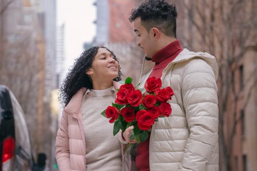 Free A couple shares a romantic moment with red roses on a city street during winter. Stock Photo