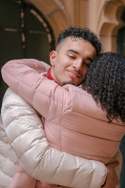 Hispanic boyfriend with closed eyes embracing girlfriend while standing close and enjoying romantic moments