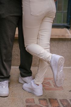 Crop anonymous female standing with raised leg while hugging boyfriend on street in daylight