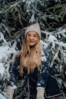 A cheerful woman standing in a snowy forest in Germany, wearing a cozy winter outfit.