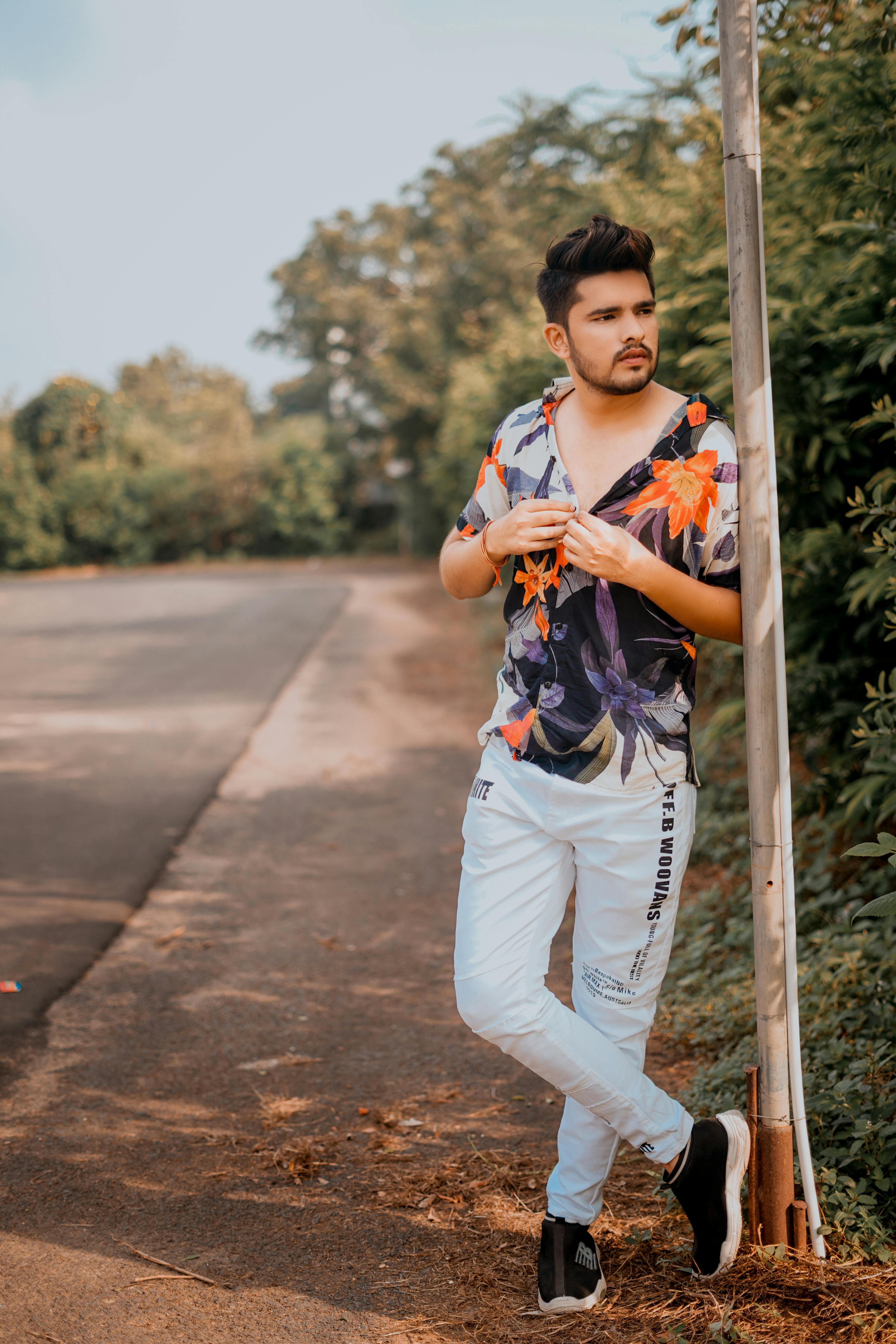 Casual portrait of a young man in a floral shirt leaning against a pole, outdoors in Ahmedabad.