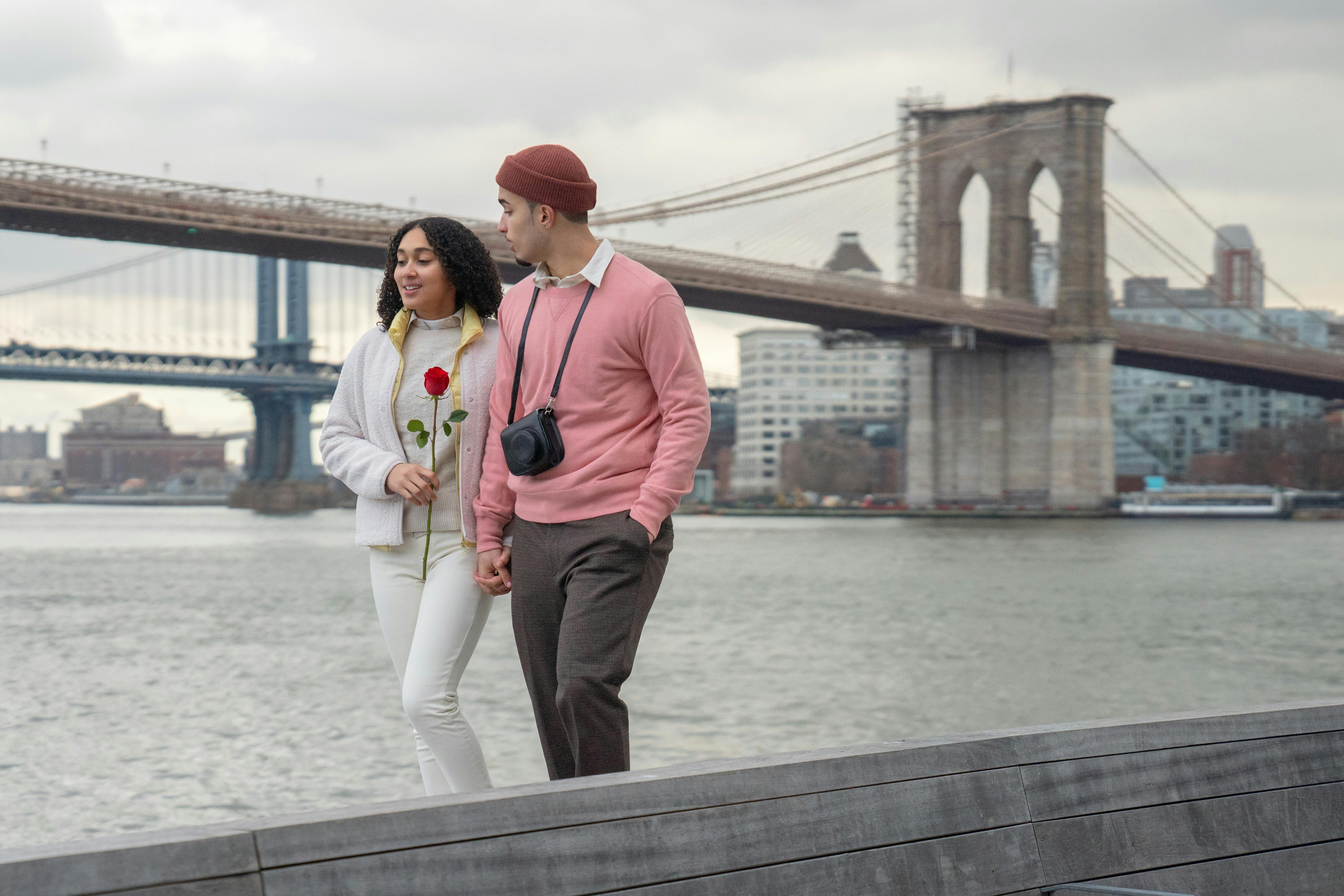 A couple walking by the Brooklyn Bridge, with romance in the air and a red rose in hand.
