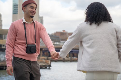 Free Cheerful Hispanic man and anonymous girlfriend holding hands on embankment Stock Photo