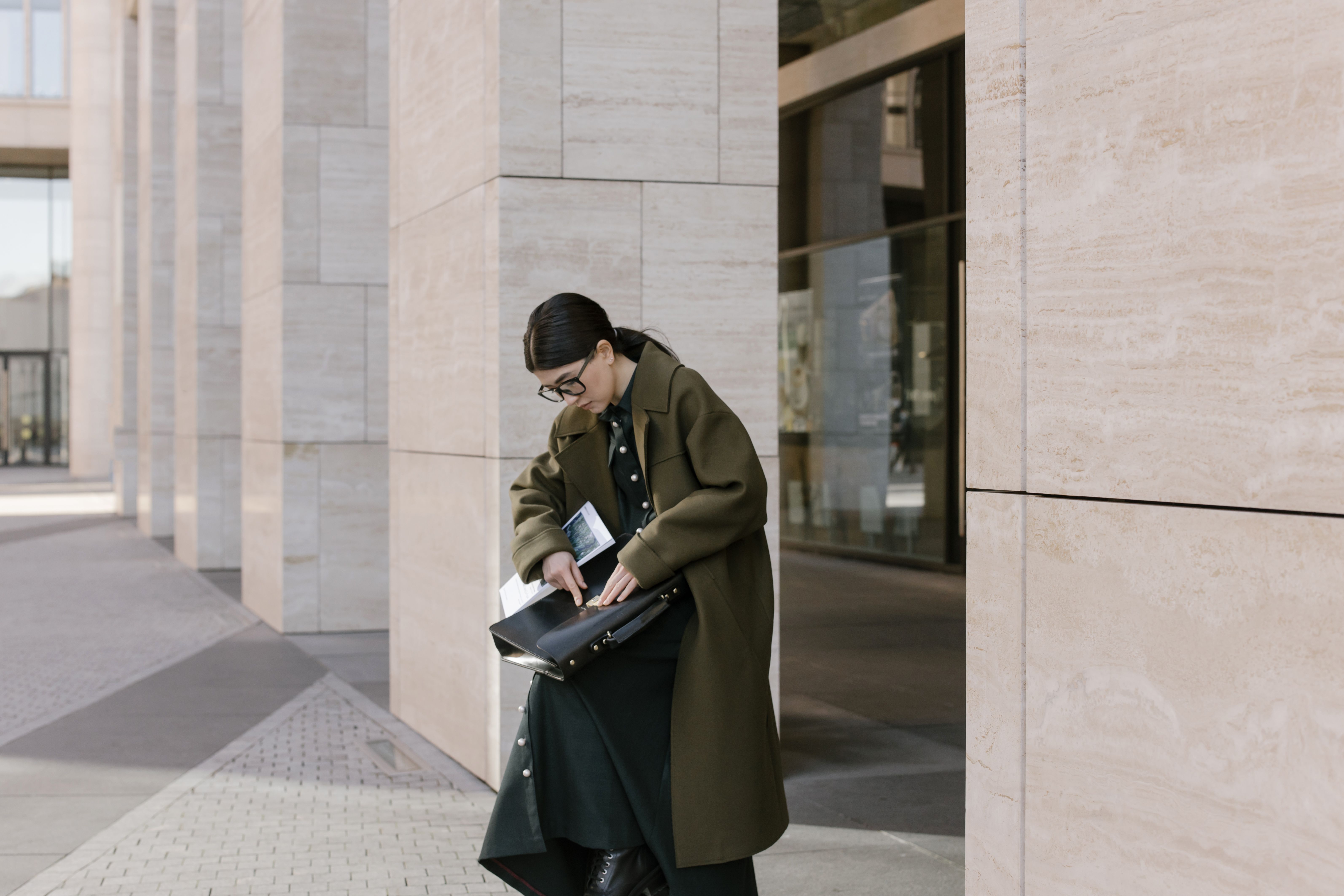 Professional woman in coat opening briefcase outdoors in urban setting.