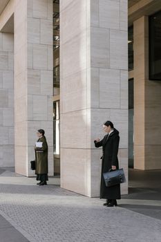 Two professional women with briefcases stand near modern architecture outdoors.