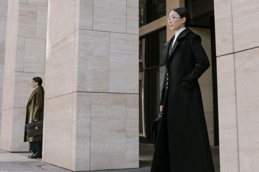 Two young professionals stand outside an office building, exuding confidence and style.