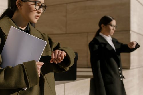 Free Two businesswomen wearing coats, checking time in bright daylight. Stock Photo