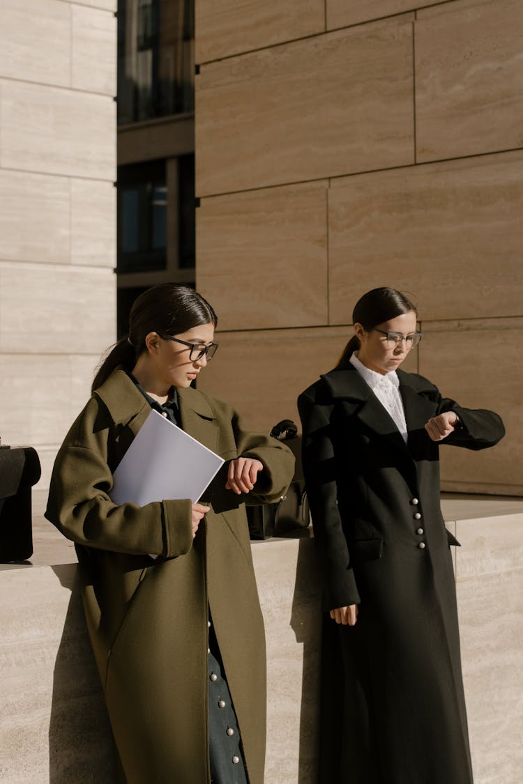 A Pair Of Women Synchronously Looking At Their Wrists