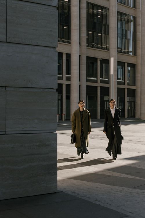 Free Two professionals walking together outside a modern office building during daytime, carrying briefcases. Stock Photo