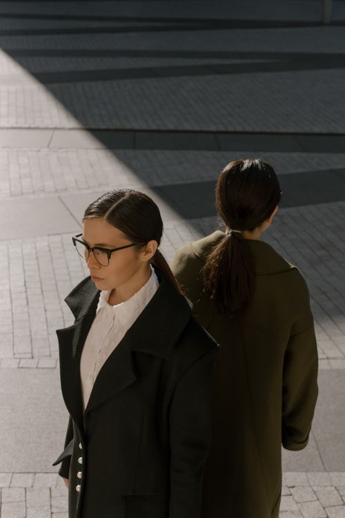 Free Two women in coats and eyewear stand in an angular urban setting with dramatic lighting. Stock Photo