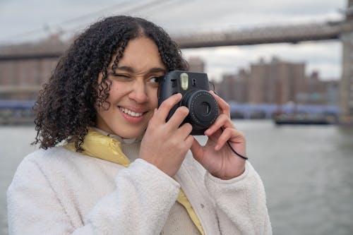 Free Hispanic female photographer with photo camera near river and bridge Stock Photo
