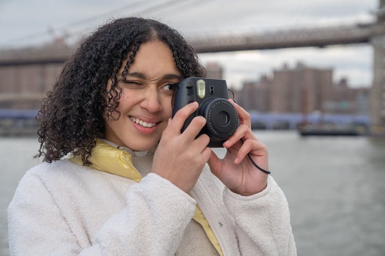 Hispanic Female Photographer With Photo Camera Near River And Bridge