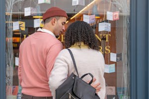 Back view of young Hispanic couple in stylish clothes cuddling while standing near glass showcase of bookstore during weekend in city