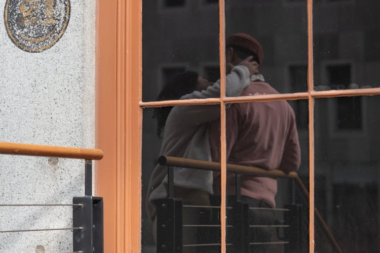 Reflection In Building Window Of Anonymous Couple Hugging On Street