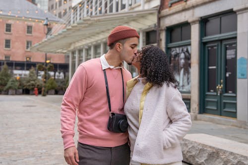 Romantic Hispanic couple in casual wear kissing while caressing on paved sidewalk on street near residential building during romantic date in city