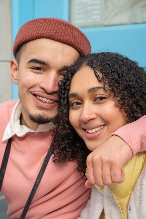 Free Happy Hispanic couple in casual wear embracing and looking at camera while sitting on street near building during romantic date Stock Photo