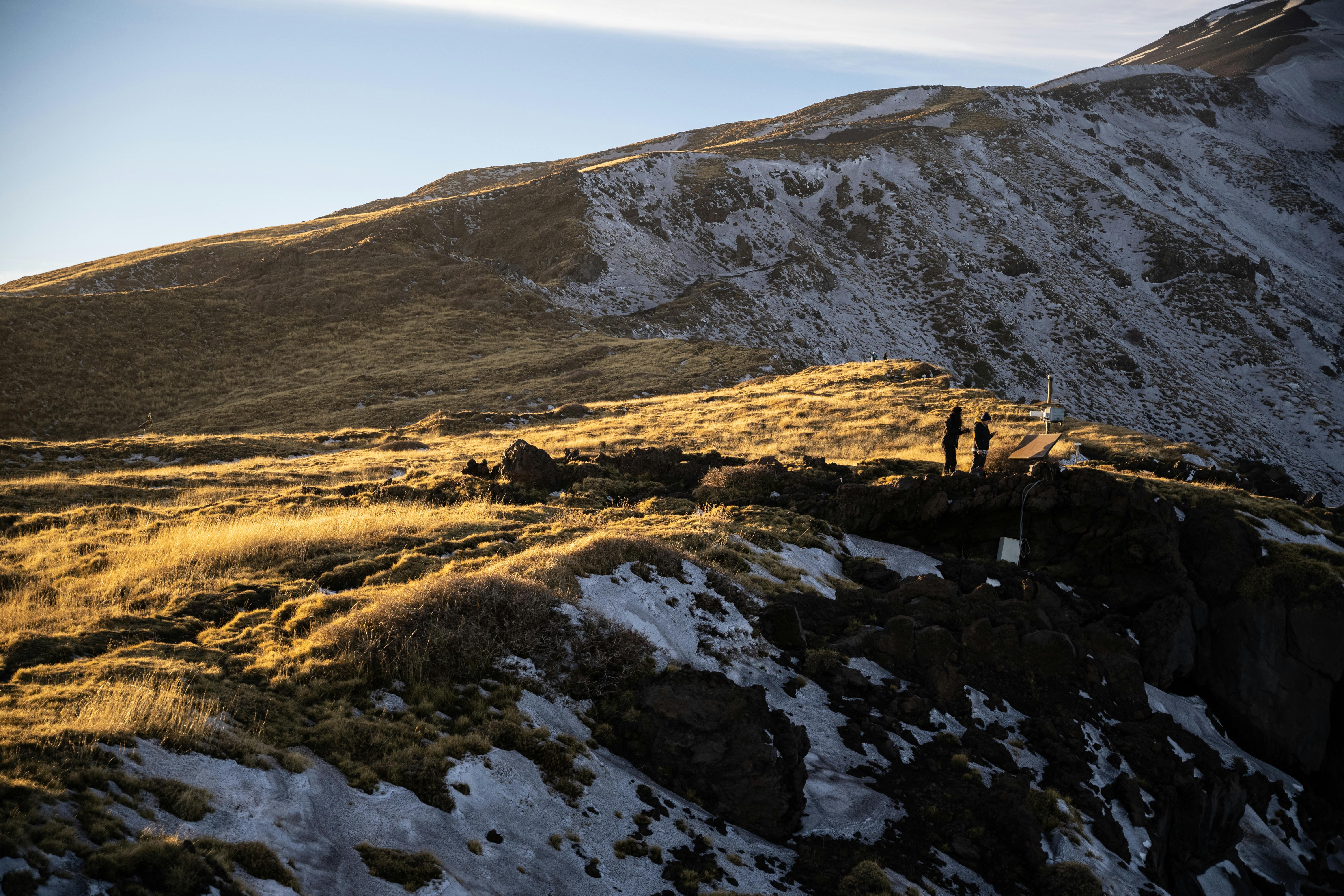 Prescription Goggle Inserts - Two people enjoy a scenic view of snow-capped mountains and sunlit grassy slopes at twilight.