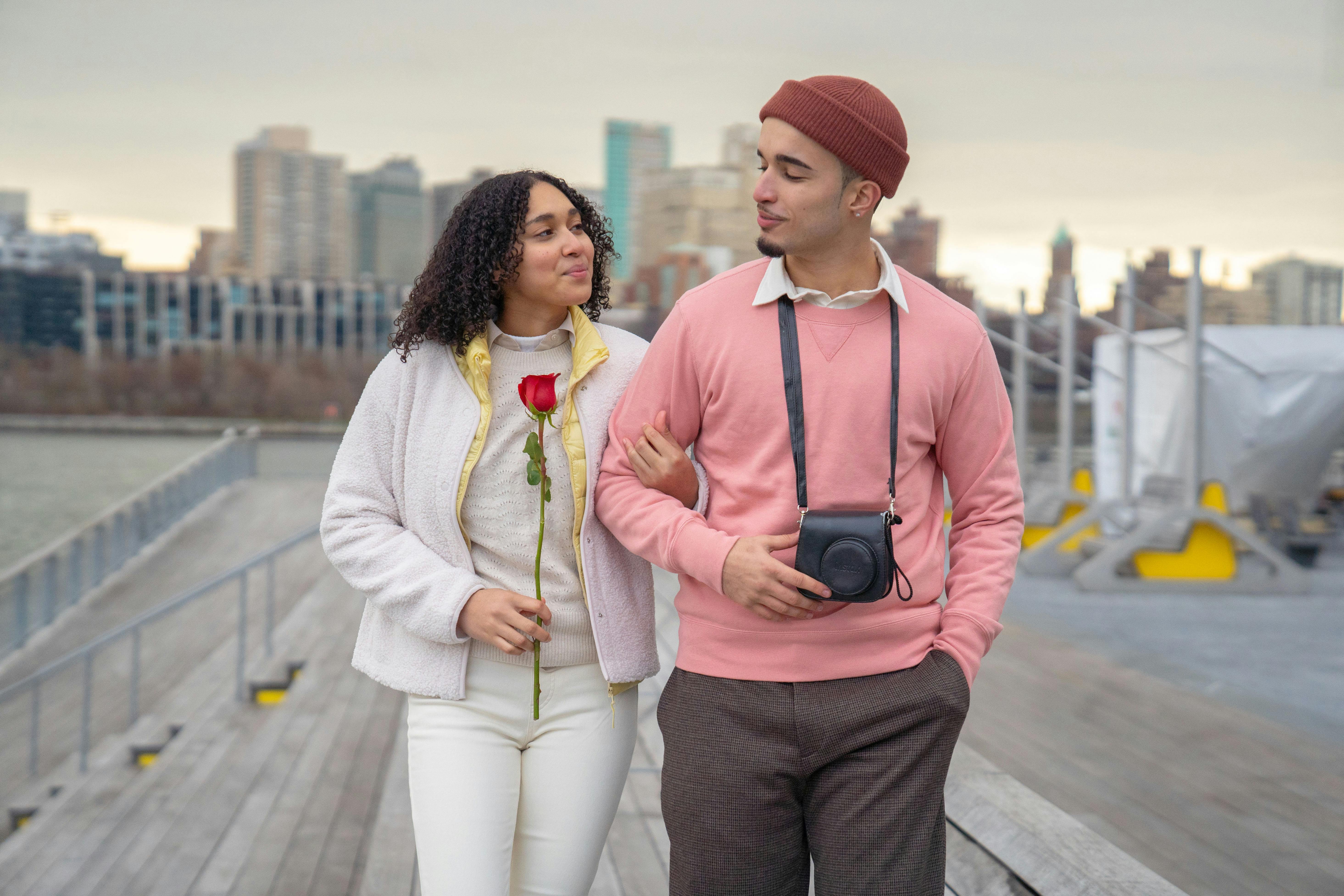 Young couple enjoys a romantic walk on a city pier with a single rose.