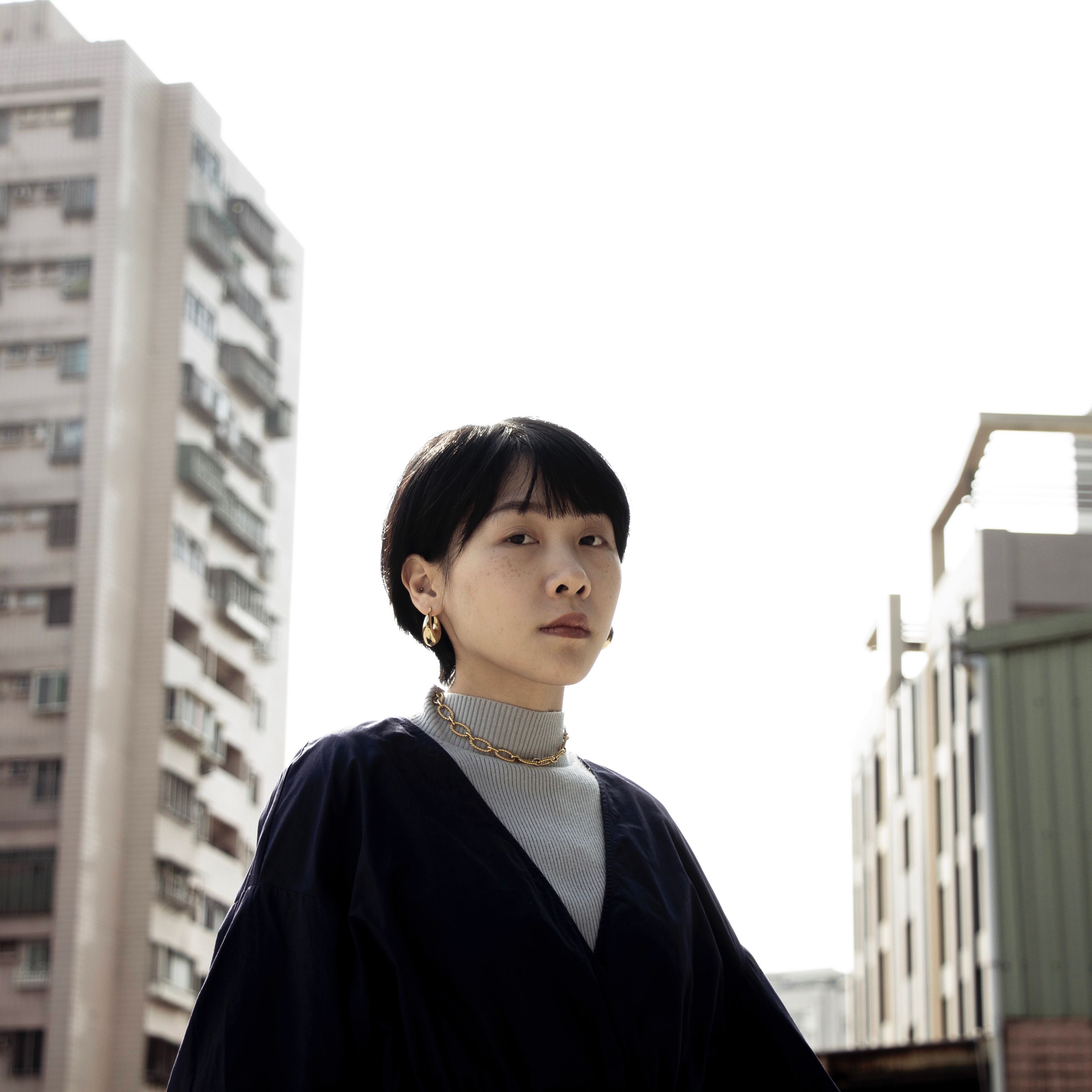 Portrait of a fashionable woman standing amidst urban buildings under bright daylight.
