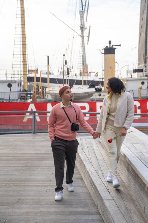 Cheerful Hispanic couple holding hands and walking on pier