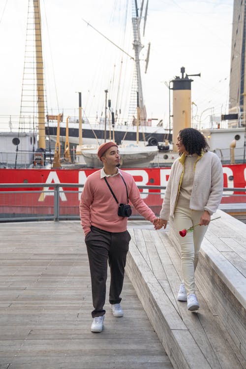 Free Cheerful Hispanic couple holding hands and walking on pier Stock Photo