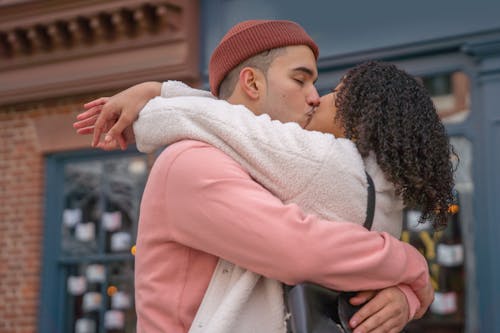 Free Side view of happy romantic ethnic couple with eyes closed kissing each other on blurred background of urban building Stock Photo