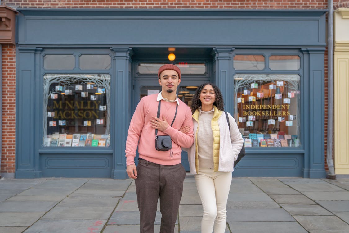 Free Cheerful young ethnic couple with photo camera smiling and looking at camera near urban building Stock Photo