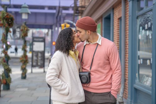 Free Side view of beloved young ethnic couple in trendy outfits kissing each other standing on city street Stock Photo