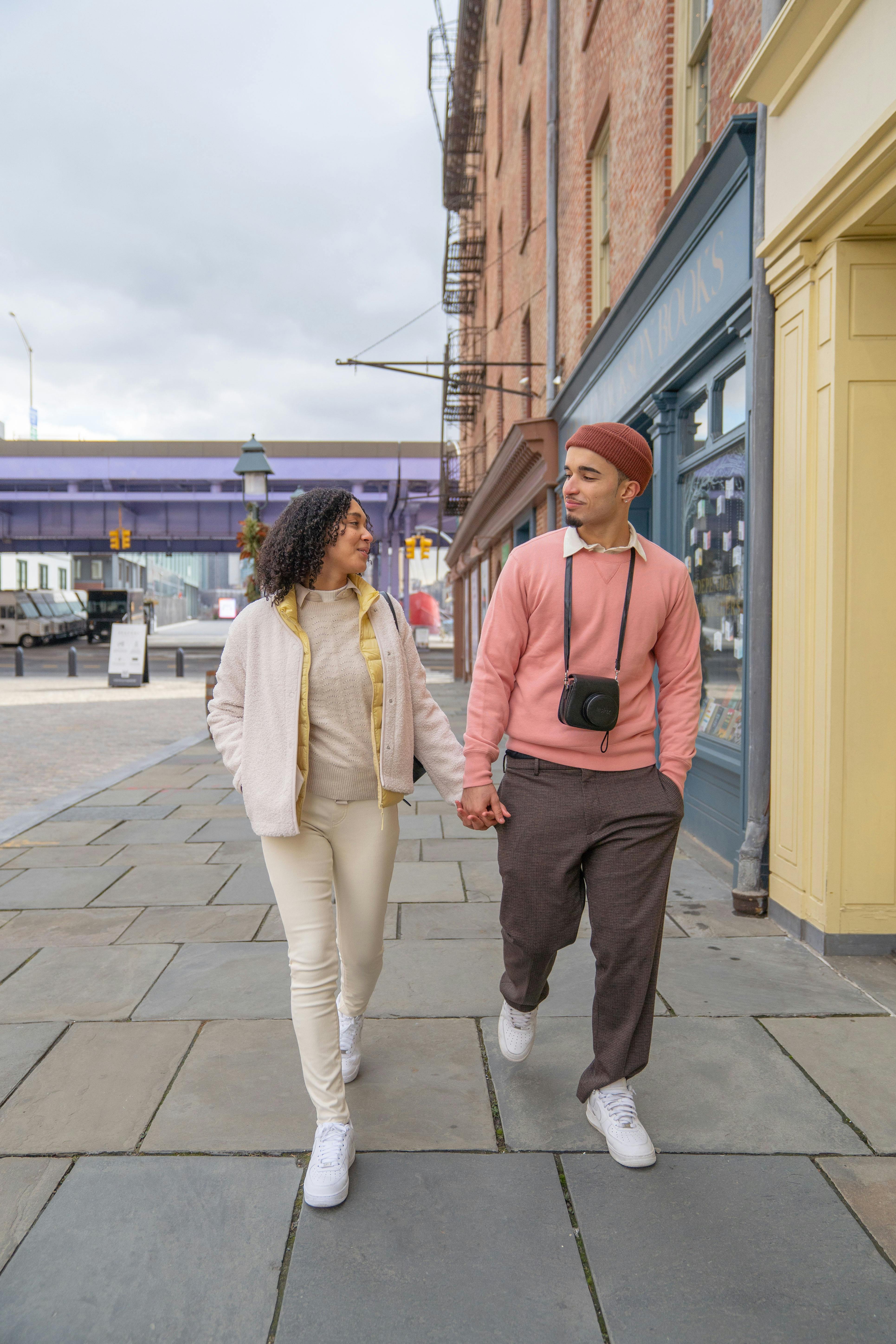 trendy young ethnic couple holding hands while walking along street