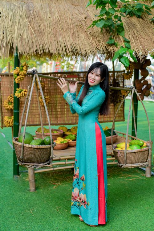 Free Woman in traditional dress standing by fruit baskets outdoors with a smile. Stock Photo